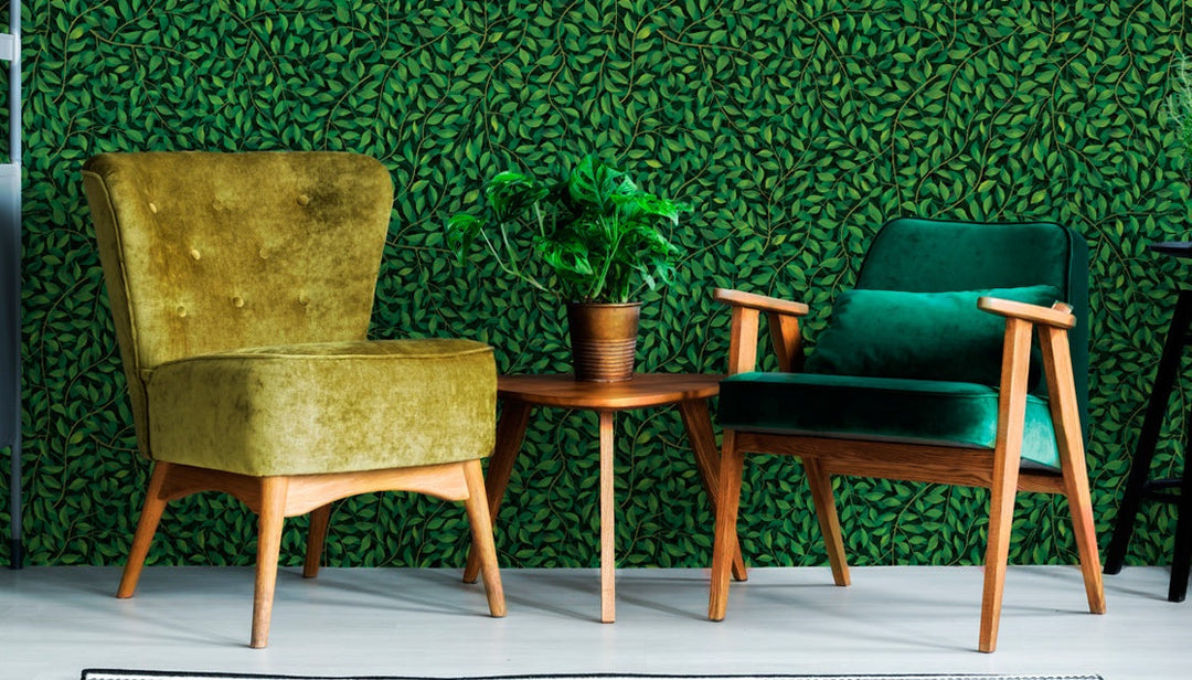 Dark leaf print wallpaper with green leafy pattern behind vintage chairs and wooden table with plant